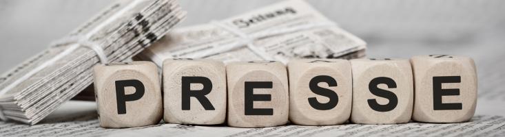 Pressebereich Holzwürfel mit Buchstaben vor einem Zeitungsstapel
