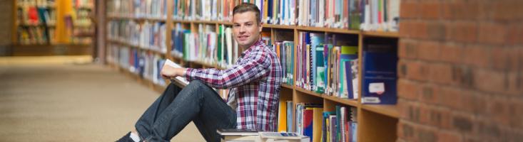 Student mit Büchern am Boden vor einem Regal sitzend