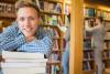 Student in der Bibliothek auf Bücherstapel lehnend